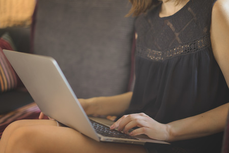 Young female freelancer working at her laptop sitting on a comfortable sofa. Modern job concept.の写真素材
