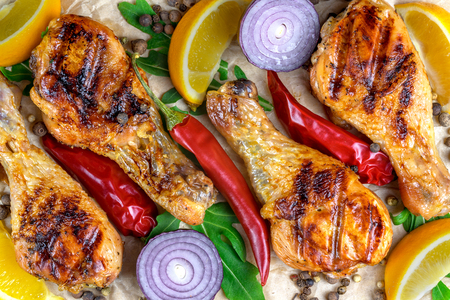 Close up of hot grilled chicken drumsticks with fresh vegetables, lemon pieces, greens and spices on rustic wooden background.の写真素材