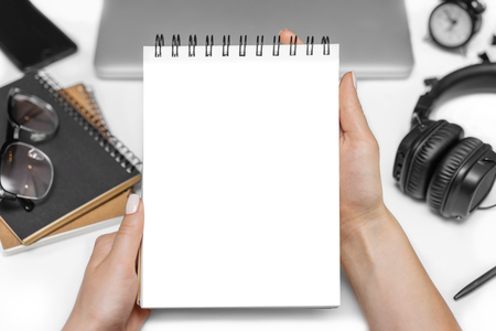 Top view of female hands holding blank sketchbook in her hands with white working desk on the backgroud. Mock up, copy space for your text.の写真素材
