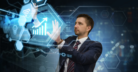Young businessman working on digital screen in futuristic virtual office choosing from financial and media info graphs. Modern business concept.の写真素材