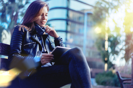 Young female student working outdoors on her project using laptop. Distant education concept. High-tech building on the background. の写真素材