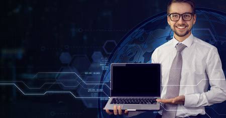 Young smiling male businessman holding in his hands laptop with blank black screen. Futuristic virtual  background. Mock up, copy space for your text. Business, finance, innovations and future techologies concept.の写真素材
