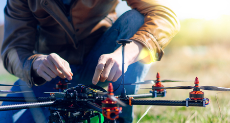 Close up cropped photo of a man sitting near generic design drone doing some adjustments before running it into the sky. Active timespending at sunny day. の写真素材