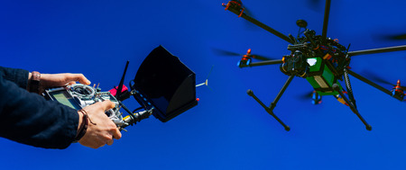 Close up of male hands holding generic design quadrocopter remote controller runing it into the sky. Cropped shot of man adjusting digital telemetry radio system. Active timespending at sunny day. の写真素材