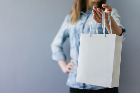 Cropped shot of female hands holding blank white paper bag in her hand. Front view, horizontal. Mock up, copy space for your text or logo.の写真素材