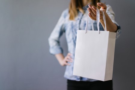 Cropped shot of female hands holding blank white paper bag in her hand. Front view, horizontal. Mock up, copy space for your text or logo.の写真素材