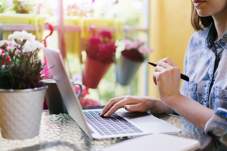 Cropped shot of casual dressed freelancer sitting on sunny terrace and working using laptop browsing some information for her new project. Distand work and education in comfortable conditions concept. Horizontal. Copy space for your text.の写真素材