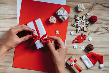 Closeup of female hands wrapping gift box on wooden background with pine tree decorations. Top view, flat lay.の写真素材
