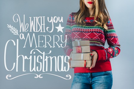 Blonde girl in red knitted sweater with christmas pattern holding bunch of gift boxes wrapped in craft paper and decorated with satin ribbon. Hand drawn x-mas wishes.の写真素材