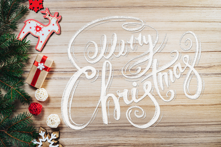 Holiday composition. Border of new year pine tree branches, new year decorarions, toys and gifts on wooden backround with Merry Christmas wishes written with calligraphic font. Top view, flat lay.の写真素材