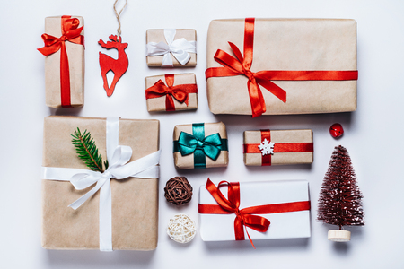 Christmas composition of various gift boxes wrapped in craft and white paper and decorated with satin red ribbons. Top view, flat lay. White background.の写真素材