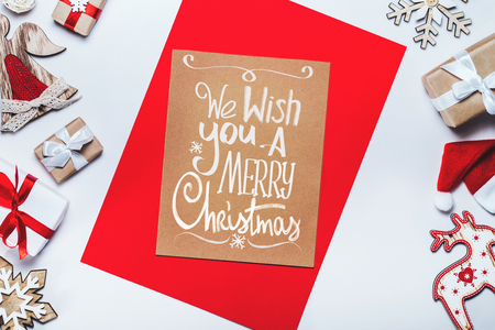 Holiday composition. Border of new year decorarions and gifts on white backround with Merry Christmas wishes written with handdrawn font on craft paper piece. Top view, flat lay.の写真素材