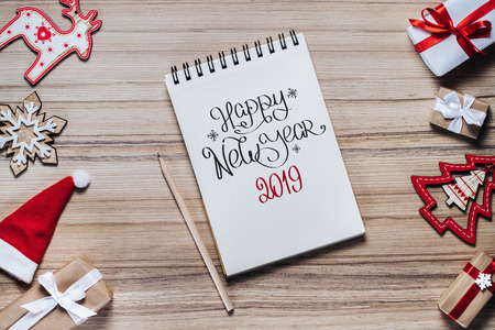 Border of holiday decorations, toys and gift boxes on wooden background. Sketchbook with a pencil to write best wishes. Hand drawn text with x-mas congratulations. Christmas composition. Top view, flat lay.の写真素材
