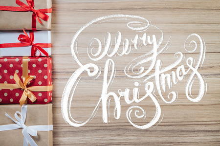 Holiday composition. Border of various new year gifts on wooden backround with Merry Christmas wishes written with calligraphic font. Top view, flat lay.の写真素材
