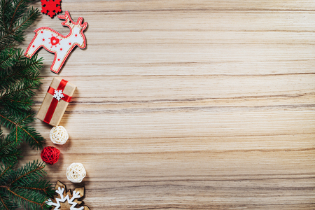 Christmas composition. Border of pine tree branches with holiday decorations and gift box wrapped in craft paper and decorated with red satin ribbon on wooden background. Top view, flat lay. Mockup, copyspace for your text.の写真素材