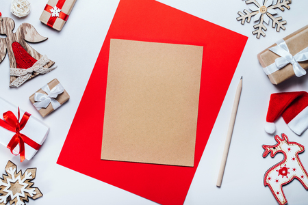 Border of christmas decorations and gift boxes with blank piece of craft paper to write holiday wishes. Top view, flat lay. Mockup, copy space for your text.の写真素材