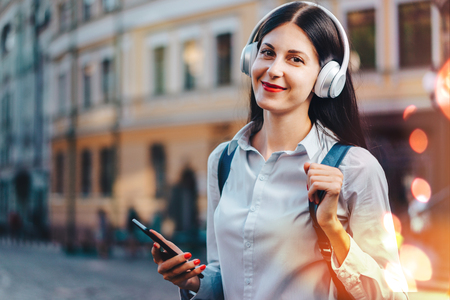 Young pretty long haired tourist girl with a backpack enjoying the walk through the old city street and listening to music.の写真素材