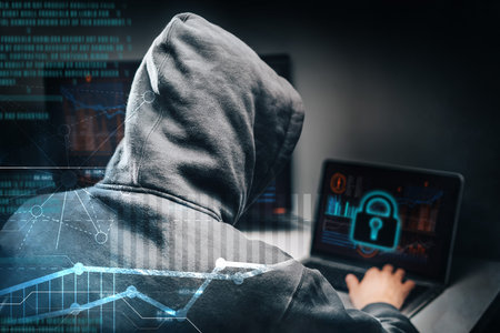 Male hooded hacker with hidden face accessing to personal information on a computer in the dark....