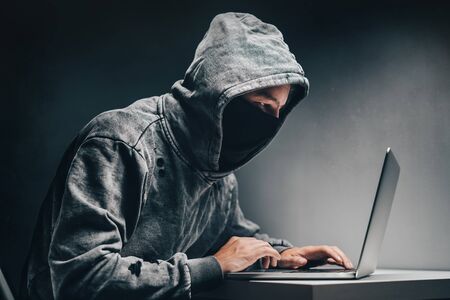 Male hooded hacker with hidden face accessing to personal information on laptop in the dark. Technologal, cyber crime concept.の写真素材