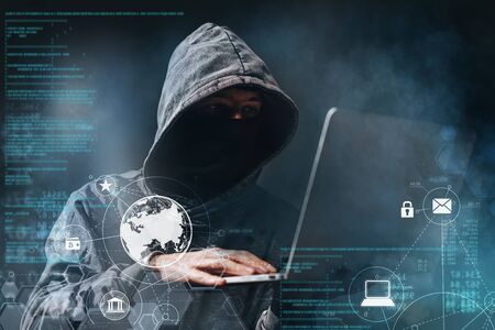 Male hooded hacker with hidden face accessing to personal information on laptop in the dark. Technologal, cyber crime concept.の写真素材