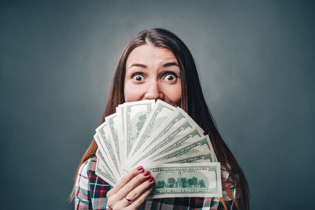 Young attractive woman showing sincere emotions of excitement and happiness with dollar banknotes in hands. Money win concept.の写真素材