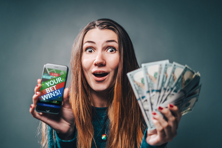 Young attractive woman showing sincere excitement about victory in online lottery. Girl being happy winning a bet in online sport gambling application on her mobile phone.の写真素材