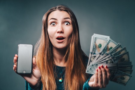 Young attractive woman showing sincere excitement about victory in online lottery. Girl being happy winning a bet in online sport gambling application on her mobile phone.の写真素材