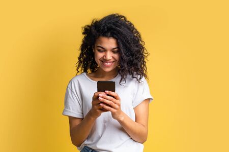 Cute happy blogger girl with perfect smile in basic white t-shirt using her mobile phone answering to her followers, texting to her boyfriend, browsing various applcations. Device addiction concept.の写真素材