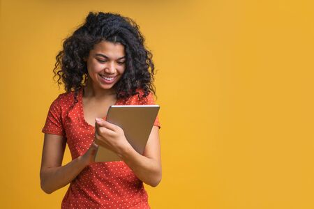 Smiling young casually dressed female entrepreneur working distantly using her tablet. Student girl preparing to exams isolated on bright colored yellow background. Copy space for your text or logo.の写真素材
