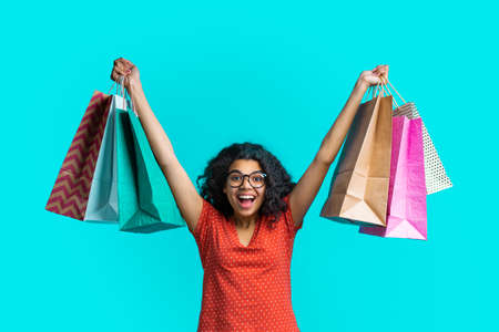 Emotional dark skinned girl with bunches of shopping bags showing sincere excitement getting her purchases at a very favorable priceの写真素材