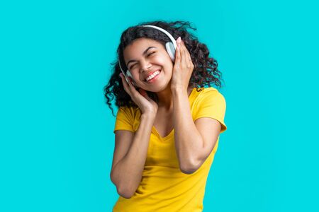 Half length portrait of casually dressed cute girl chilling, enjoying listening to music via wireless headset, dancing over bright colored blue backgroundの写真素材