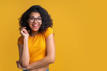 Portrait of young attractive dark skinned woman wearing crop top and trendy spectacles. Cute coquette girl posing on bright colored yellow background. Copy space for your text.の写真素材