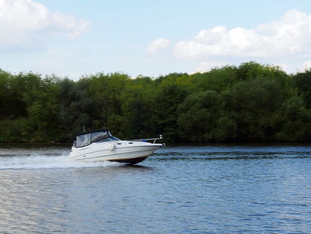 The pleasure boat quickly sails along the river against the background of the Bank overgrown with...