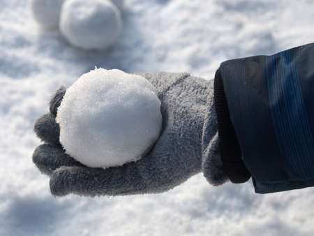 A child's gloved hand holds a snowball on a white snow background. Outdoor activities, outdoor games, winter entertainment.の写真素材