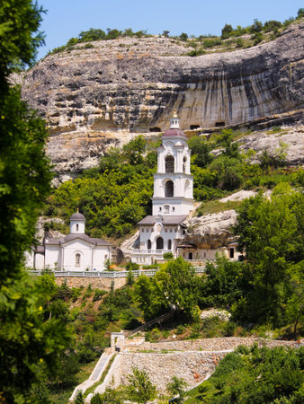 A Christian monastery in the mountains, a bell tower with a rock hanging over it against the blue...