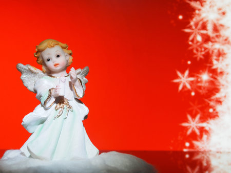 An angel holding a candle in his hand, a clay figure on a red background, a symbol of Christmas....