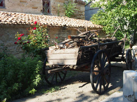 An old cart loaded with firewood in a green garden against the background of stone walls. Details of the garden interior, decoration in a rural style.の写真素材
