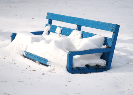 Blue wooden bench covered with snow in the park. Winter background.