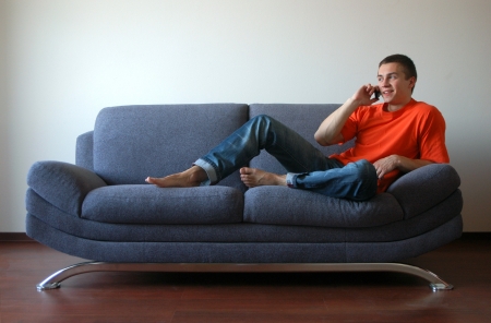 Sexy young man talking on the cell phone sitting on the sofaの写真素材