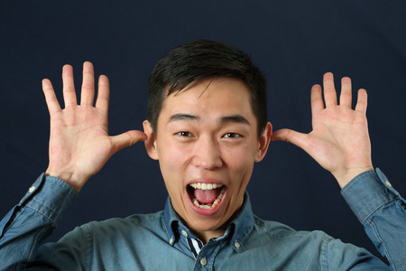 Funny young Asian man making face and looking at cameraの写真素材