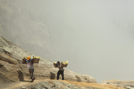 KAWAH IJEN, INDONESIA - AUGUST 8, 2011: Miners carry baskets with sulphur in the fumes of toxic volcanic gas from the sulphur mines in the crater of the active volcano of Kawah Ijen, East Java, Indonesia.のeditorial素材