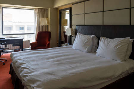 Bucharest, Romania- JUNE 14, 2019: Modern hotel or apartment bedroom with freshly made king-size bed. Under natural day light from the window. Interior design and hospitality.のeditorial素材