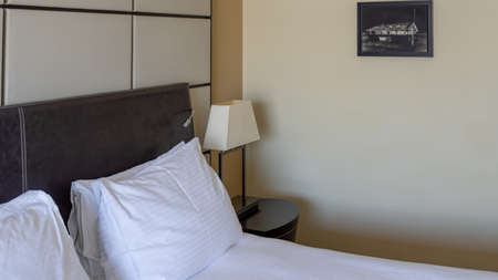 Modern interior hotel bedroom detail. Headboard, pillows, head lamp, artwork on the wall. Under natural light. Interior design and decoration.のeditorial素材