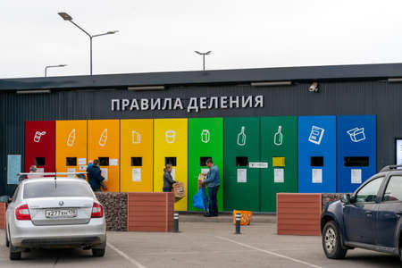 St. Petersburg, Russia- MARCH 26, 2021: Large, twice the human size different colorful waste containers set at the station near the parking lot with waste icons and people using them.のeditorial素材
