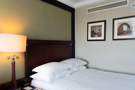 Modern interior hotel bedroom with freshly made bed, headboard, pillows, back lighting, artwork on the wallのeditorial素材
