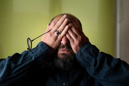 Man hides his face behind his hands so he doesn't have to see