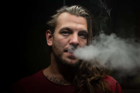 Close up of a young man exhaling a cloud of steam or smoke with an electronic cigarette.の写真素材