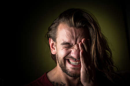 Young man with long hair covers his face while suffering from headache or migraineの写真素材