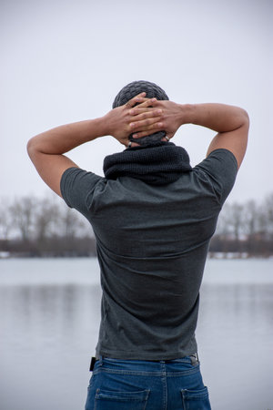 A young man is standing in a short-sleeved T-shirt on a lake. He stands with his back to the camera.の写真素材