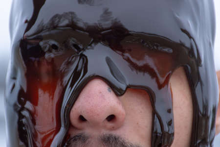 The head of a man was doused with brown syrup. His eyes are closed.の写真素材